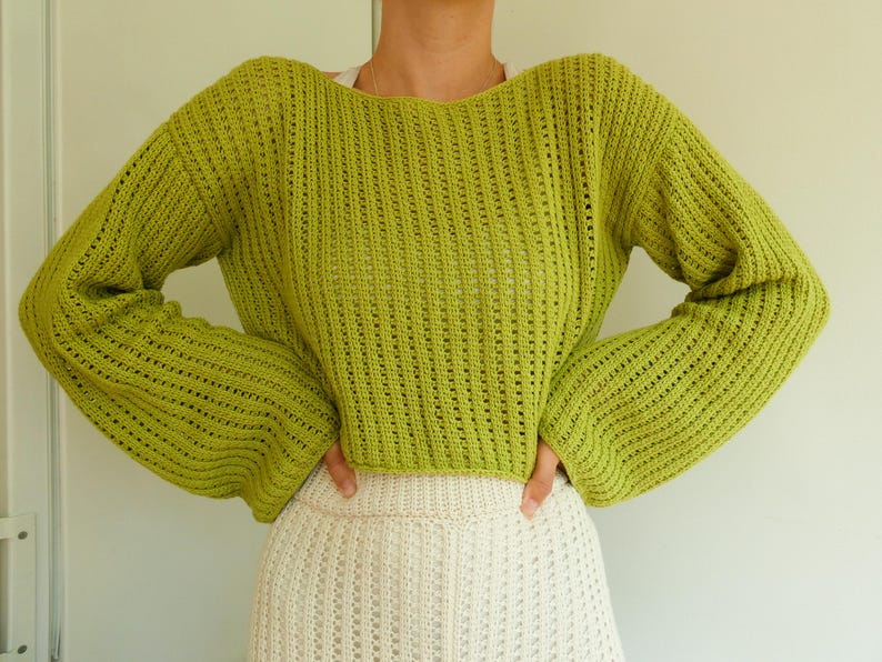May include: A lime green knitted sweater with a loose fit and long sleeves. The sweater has a slightly cropped length and a delicate open-stitch pattern.