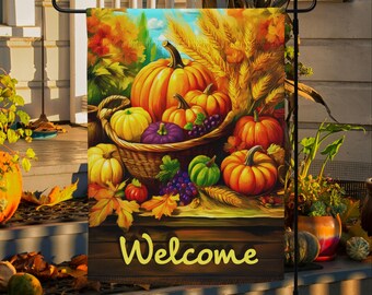 May include: A garden flag featuring a fall harvest scene with pumpkins, grapes, and wheat. The word "Welcome" is written in yellow script across the bottom. The flag is displayed on a black metal stand.