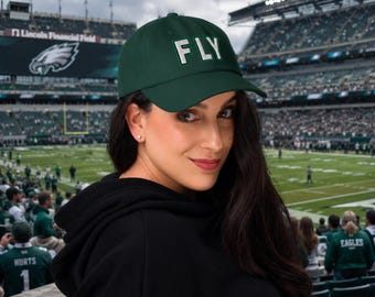 May include: A dark green baseball cap featuring the word FLY embroidered in white capital letters with a thin black outline on the front panel. The cap has a structured crown, a curved brim, and a matching green button on the top center.