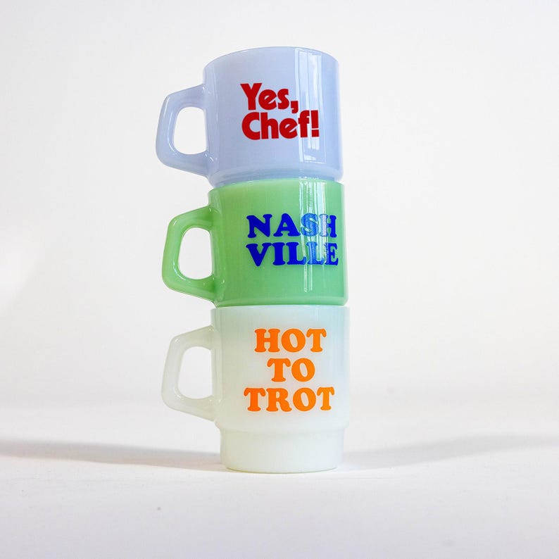 May include: Three stacked mugs with different colored glazes and text. The top mug is light blue with the text "Yes, Chef!" in red. The middle mug is green with the text "NASHVILLE" in blue. The bottom mug is white with the text "HOT TO TROT" in orange.