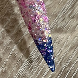 Puede incluir: Una muestra de u&ntilde;a larga y puntiaguda con un dise&ntilde;o degradado. La mitad superior es una mezcla de purpurina rosa y escamas iridiscentes, que transiciona a un azul profundo en la punta. La u&ntilde;a est&aacute; adherida a un palito de pl&aacute;stico transparente.