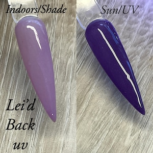 May include: Two nail polish swatches, one in shade and one in UV light. The shade swatch is a light lavender colour, while the UV swatch is a deep purple. The text "Indoors/Shade" and "Sun/UV" are at the top. The text "Lei'd Back uv" is at the bottom.