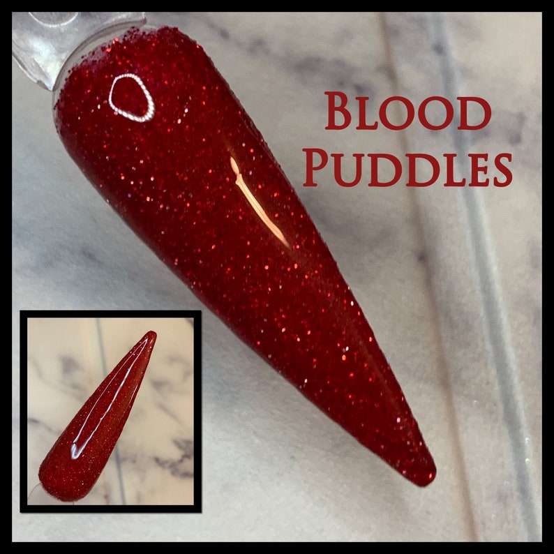 K&ouml;nnte beinhalten: Roter Glitzernagellack mit einer tief roten Farbe und einem feinen Glitzerfinish. Der Lack wird auf einem Nagelspitzen gezeigt und der Text "BLOOD PUDDLES" ist im Bild sichtbar.