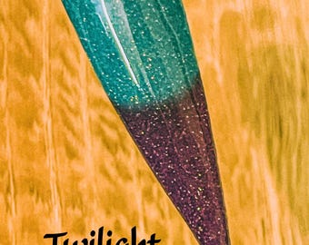 May include: A teal and purple nail polish with glitter. The polish is called "Twilight Lagoon".