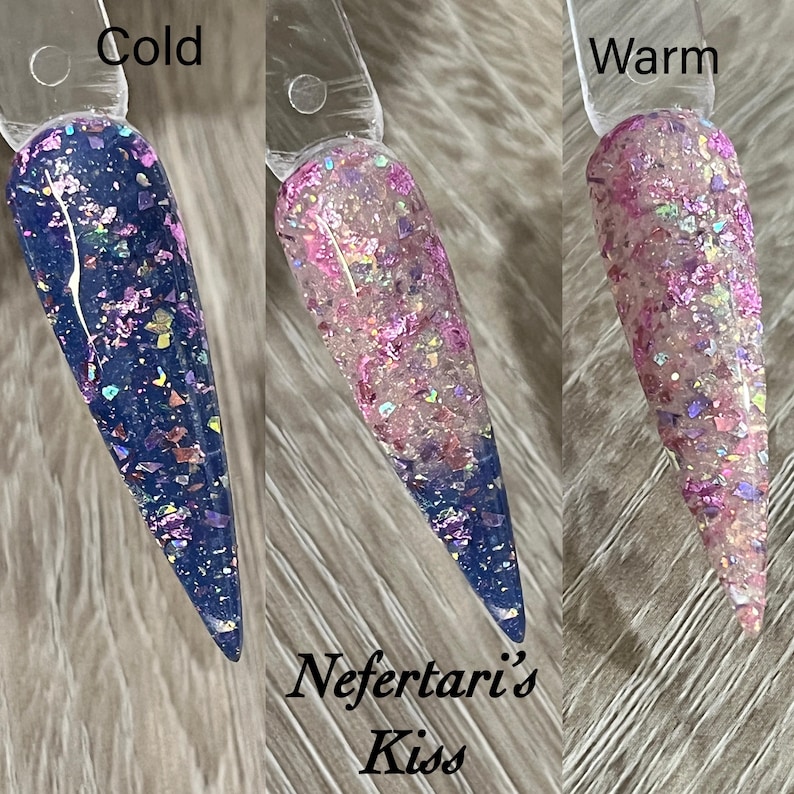 Puede incluir: Tres muestras de esmalte de u&ntilde;as que muestran cambios de color. La muestra de la izquierda es azul oscuro con purpurina iridiscente, etiquetada como "Cold". La muestra del medio es rosa y morada, y la muestra de la derecha es rosa claro, etiquetada como "Warm". El texto "Nefertari's Kiss" est&aacute; en la parte inferior.