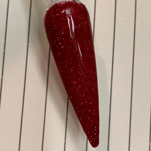 K&ouml;nnte beinhalten: Nahaufnahme eines roten Glitzer-Nagellacks auf einem klaren Nagelspitzen.