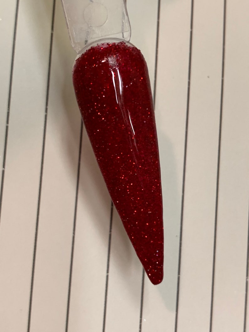 K&ouml;nnte beinhalten: Nahaufnahme eines roten Glitzer-Nagellacks auf einem klaren Nagelspitzen.