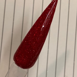 K&ouml;nnte beinhalten: Nahaufnahme eines roten Glitzer-Nagellacks auf einem durchsichtigen Applikatorstab. Der Lack hat eine feine Glitzer-Oberfl&auml;che und ist tiefrot.