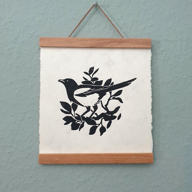 Peut inclure: Impression en silhouette noire et blanche d'une pie perch&eacute;e sur une branche, encadr&eacute;e d'un cadre en bois naturel.