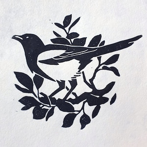 Peut inclure: Gravure sur linol&eacute;um en noir et blanc d'une pie perch&eacute;e sur une branche avec des feuilles.