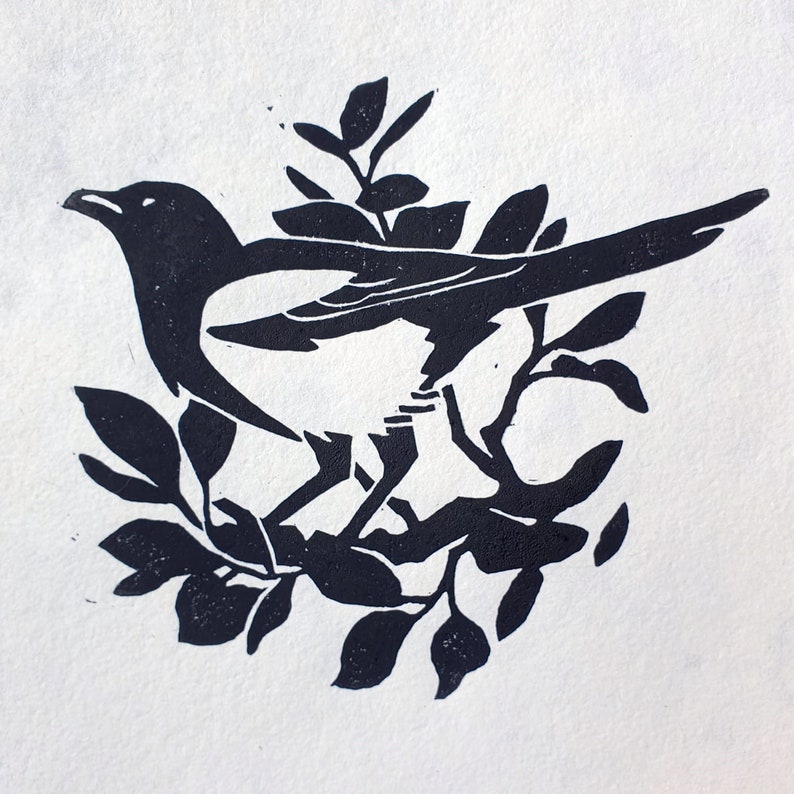 Peut inclure: Gravure sur linol&eacute;um en noir et blanc d'une pie perch&eacute;e sur une branche avec des feuilles.