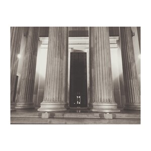 May include: A black and white photo of a building with a row of columns and a doorway in the center.