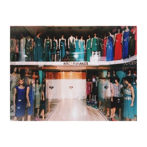 May include: A storefront with a variety of dresses on display. The dresses are in a variety of colors, including red, blue, green, and white. The storefront is decorated with a sign that says "ΑΠΟΣΤΟΛΑΚΟΣ".