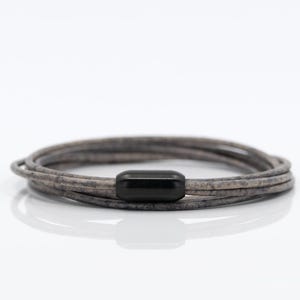 Può includere: Un braccialetto multistrato in pelle grigia con una chiusura in metallo nero.