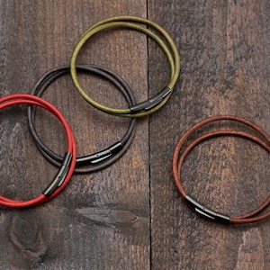 May include: Four leather bracelets with black metal clasps. The bracelets are in different colors: green, brown, black, and red.