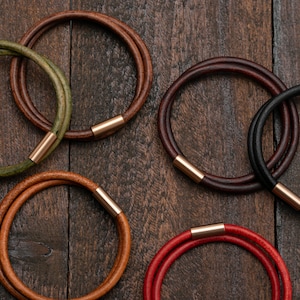 May include: Six leather bracelets with gold-toned clasps. The bracelets are in various colors, including brown, green, black, and red.