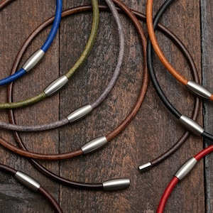 May include: A collection of leather cord necklaces with magnetic clasps in various colours, including blue, green, grey, brown, black, and red.