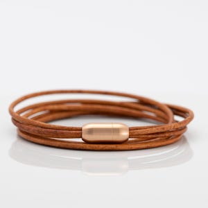 Può includere: Un braccialetto avvolgente in pelle marrone con chiusura magnetica dorata.