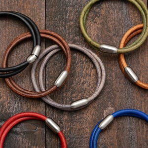 May include: Six leather bracelets with silver magnetic clasps. The bracelets are in various colors, including black, brown, gray, green, red, and blue.
