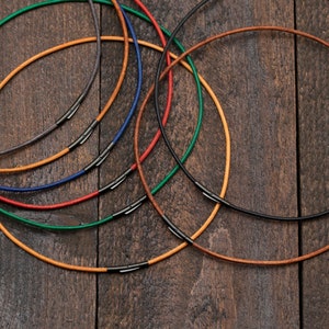 Könnte beinhalten: Ein Set aus sieben Lederkordelketten in verschiedenen Farben, darunter Braun, Rot, Grün, Blau und Schwarz. Jede Kette hat einen silbernen Verschluss.