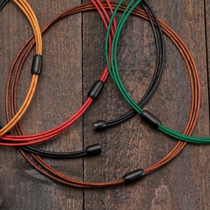May include: Four leather cords in brown, red, green, and black colours are intertwined and knotted together. The cords are arranged in a circle shape, with the ends of the cords tied together.