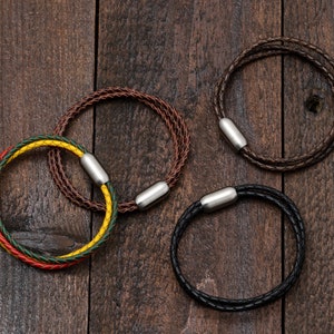 May include: Three leather bracelets with metal clasps. One bracelet is brown, one is black, and one is multi-coloured with red, yellow, and green.