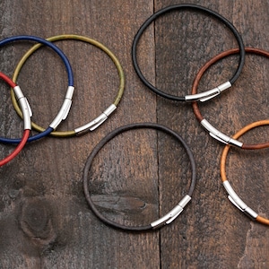 Könnte beinhalten: Fünf Lederarmbänder mit silbernen Verschlüssen. Die Armbänder sind in verschiedenen Farben: rot, blau, grün, braun und schwarz.