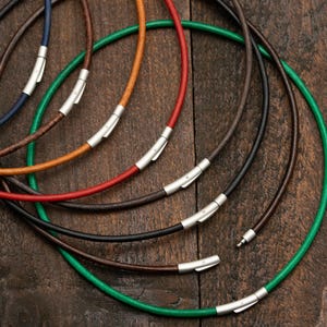 Könnte beinhalten: Ein Set aus acht Lederkordelketten in verschiedenen Farben, darunter Grün, Braun, Schwarz und Rot. Jede Kette hat einen silbernen Verschluss.