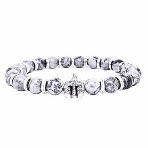 May include: A beaded bracelet featuring gray and white patterned stone beads. The bracelet includes a silver-colored Spartan helmet charm. Silver-colored spacers are between the stone beads. The bracelet is on a white background.