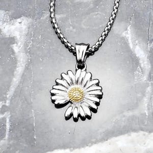 Puede incluir: Un collar de cadena de plata con un colgante de margarita de plata y oro. La margarita tiene un centro de oro texturizado.