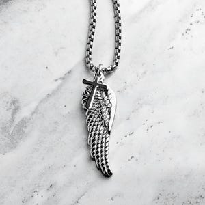 May include: A silver chain necklace with a pendant featuring a silver wing with a black cross on top.