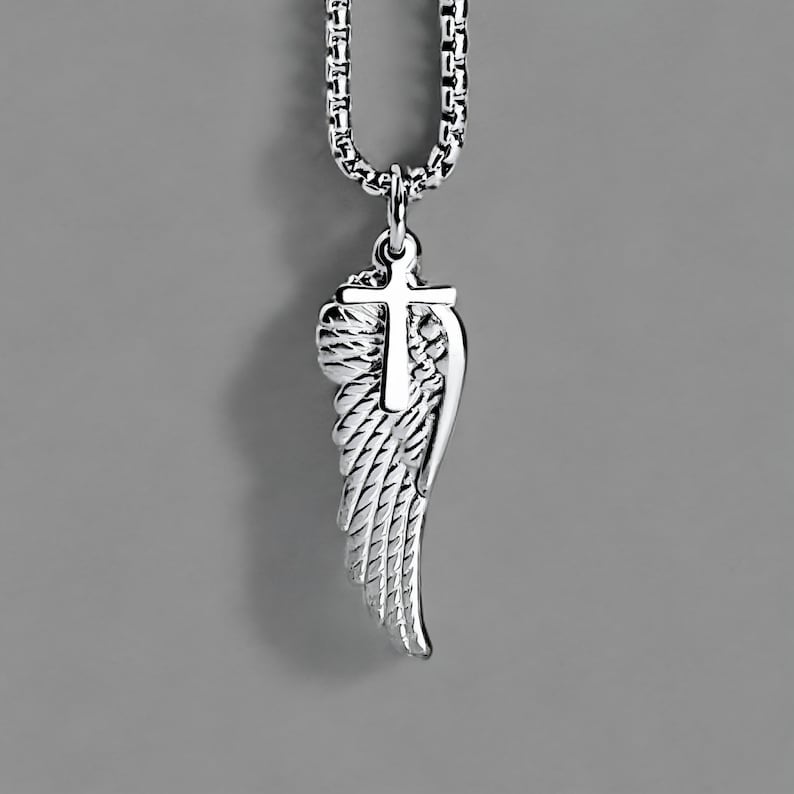 May include: A silver pendant necklace with a cross and angel wing design. The pendant is suspended from a box link chain. The wing has detailed feathering, and the cross is positioned above the wing.