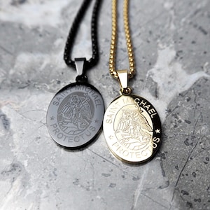Puede incluir: Dos colgantes ovalados con un diseño de San Miguel. Un colgante es dorado con una cadena dorada, y el otro es negro con una cadena negra. Ambos colgantes tienen las palabras "Saint Michael Protectus" alrededor del borde.