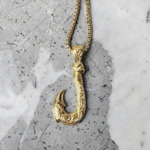 May include: A gold-tone necklace with a detailed fish hook pendant. The chain is a box chain style.