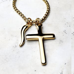 Puede incluir: Un collar de cadena dorada con un colgante de cruz dorada y un dije de chile dorado.
