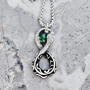 May include: Silver snake pendant necklace with a green gemstone in the center. The snake is coiled in the shape of an infinity symbol.