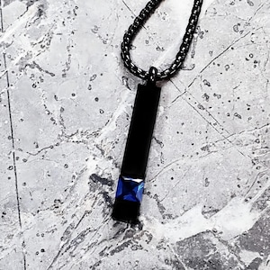 Könnte beinhalten: Eine schwarze Kettenkette mit einem schwarzen Anhänger mit einem blauen quadratischen Edelstein.
