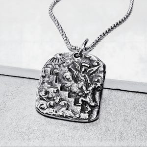 Puede incluir: Un collar de plata con un colgante que presenta un diseño detallado de un ángel ascendiendo una escalera con nubes y un sol radiante en el fondo.