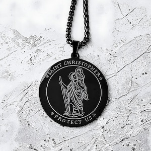 May include: Black Saint Christopher pendant necklace. The round pendant features an engraved image of Saint Christopher carrying a child, with the words "SAINT CHRISTOPHER" and "PROTECT US" around the edge. The necklace has a black chain.