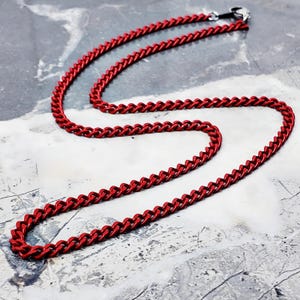 May include: A red chain necklace with a lobster clasp. The necklace is made of small, interlocking links. The chain is a vibrant red color and is displayed on a gray and white surface.