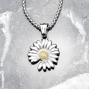 May include: A silver chain necklace with a silver daisy pendant. The daisy has a gold center.