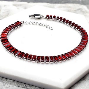 Op de afbeelding: Een zilveren armband met een rij rode rechthoekige edelstenen.