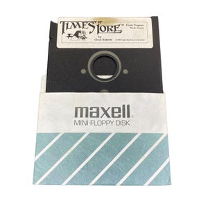 May include: A black 5.25-inch floppy disk labeled "Times of Lore" by Chris Roberts, with a Maxell Mini-Floppy Disk sleeve. The sleeve is white with blue diagonal stripes.