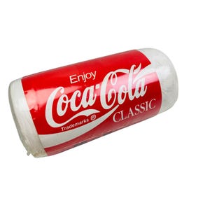 以下が含まれることがあります： 赤と白のCoca-Cola Classicパッケージで包まれた円筒形の物体。パッケージには、白いスクリプトのCoca-Colaロゴ、ロゴの上に「Enjoy」、下に「CLASSIC」という文字が記載されています。物体は白です。