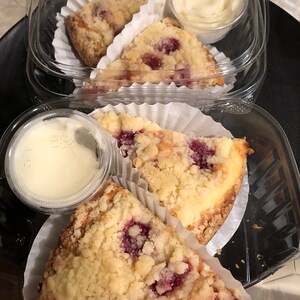 May include: Three slices of raspberry crumble dessert in individual containers with a small container of whipped cream on the side.