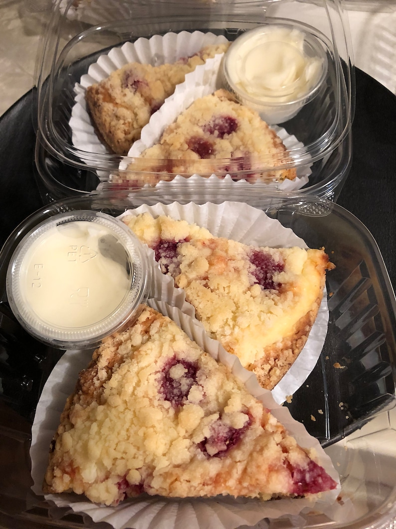 May include: Three slices of raspberry crumble dessert in individual containers with a small container of whipped cream on the side.