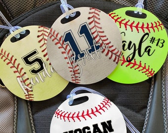 May include: Three round baseball-themed luggage tags with white, yellow, and green backgrounds. The tags have red stitching and a white loop for attaching to luggage. The tags are personalized with names and numbers: "Kendall #5", "Braxton #11", and "Ayla #13".