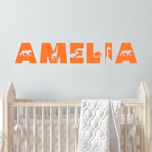 Peut inclure: Autocollant mural orange avec le nom "AMELIA" &eacute;crit en grandes lettres. Chaque lettre est remplie d'une silhouette d'animal diff&eacute;rente, notamment un lion, une girafe, une antilope, un &eacute;l&eacute;phant et une girafe.