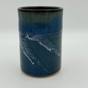 Peut inclure: Un gobelet en céramique fait à la main avec un glaçage bleu foncé et des motifs blancs texturés en forme de vagues. Le bord supérieur est de couleur vert foncé. Cette tasse cylindrique est idéale pour les boissons.