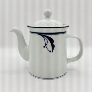 May include: A white ceramic mug with a black handle and the text "But First, Coffee" in a bold, black font. The mug is filled with a dark liquid, likely coffee, and sits on a light-colored surface.